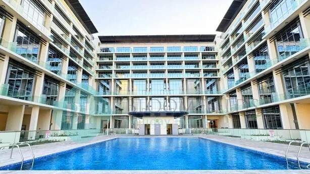 Un bâtiment moderne doté d’une piscine centrale, de nombreux balcons et de grandes fenêtres.