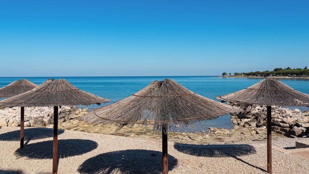 En strand med parasoller av halm och en stenig kustlinje.