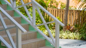 A staircase with white railings and beige steps, surrounded by greenery and a wooden fence. - The Private Garden The Ambassador (Jan Thiel)