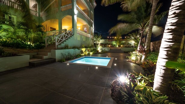 A pool area with a staircase leading to a balcony, surrounded by palm trees and plants. - The Private Garden The Ambassador (Jan Thiel)