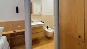 Una habitación de hotel moderna con un armario de madera, una mesita de noche, un espejo y un bidé.