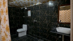 Un baño con inodoro, lavamanos y espejo. Las paredes presentan un diseño de mármol negro.