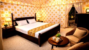 Un dormitorio con cama, mesitas de noche, una lámpara, una silla y una pequeña mesa con una taza y una planta.