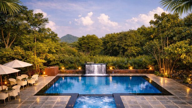 Piscina con caída de agua, rodeada de exuberante vegetación y baldosas de piedra.