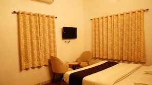 Habitación de hotel con dos camas individuales, una mesita pequeña, dos sillas y un televisor de pantalla plana en la pared.
