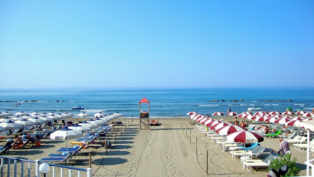 A beach with rows of sunbeds and umbrellas, a lifeguard tower, and the ocean in the background.