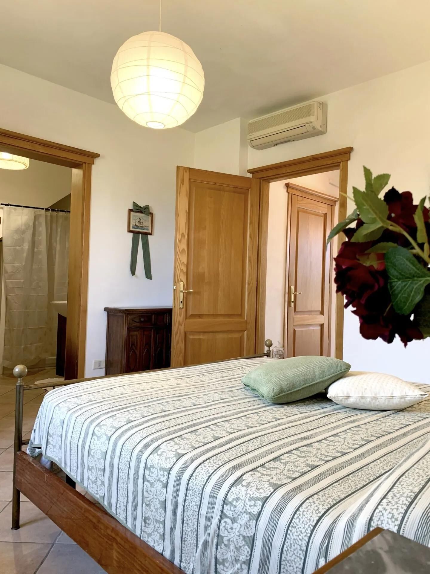 Une chambre à coucher avec un lit, un luminaire suspendu, une porte en bois et un climatiseur fixé au mur.