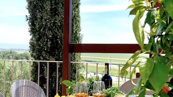 An outdoor dining area with a table set for two, featuring a bottle of wine, glasses, bread, and fruits.