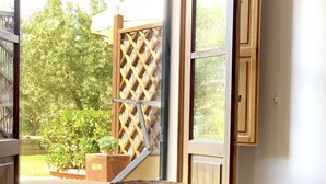 A room with a bed, a window with a view of greenery, and a wooden lattice structure outside.