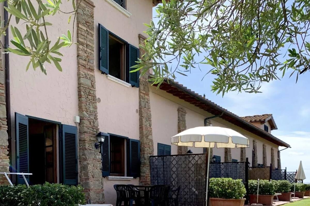 A building with stone walls and blue shutters, outdoor seating with tables and chairs, and a lawn with flowers.