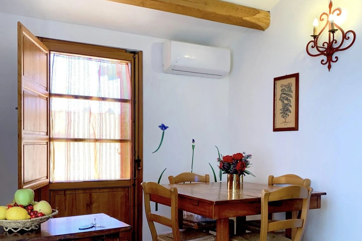 Un coin repas avec une table et des chaises en bois, une fenêtre avec des rideaux, un climatiseur fixé au mur et un tableau encadré.