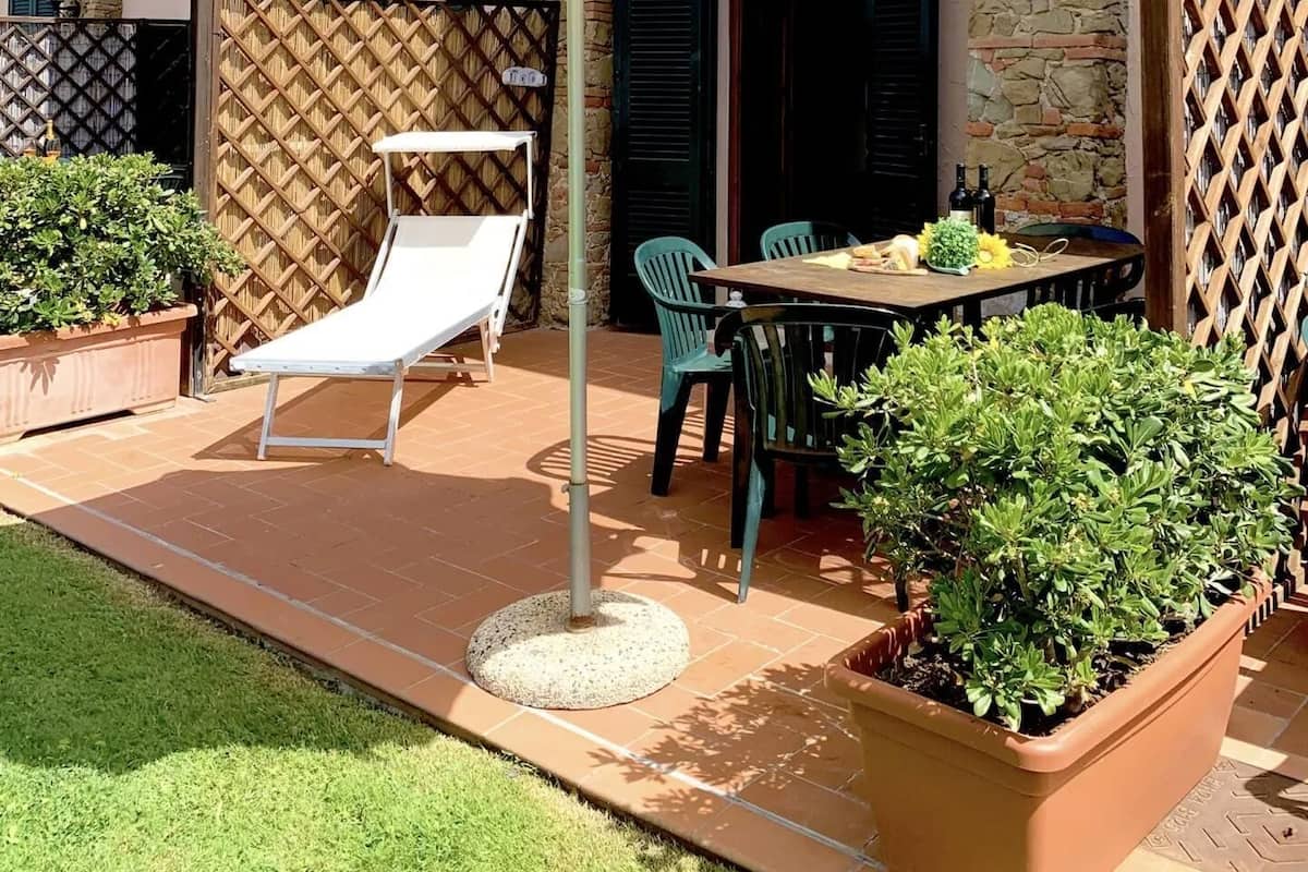 A patio with a table and chairs, a white umbrella, and potted plants.