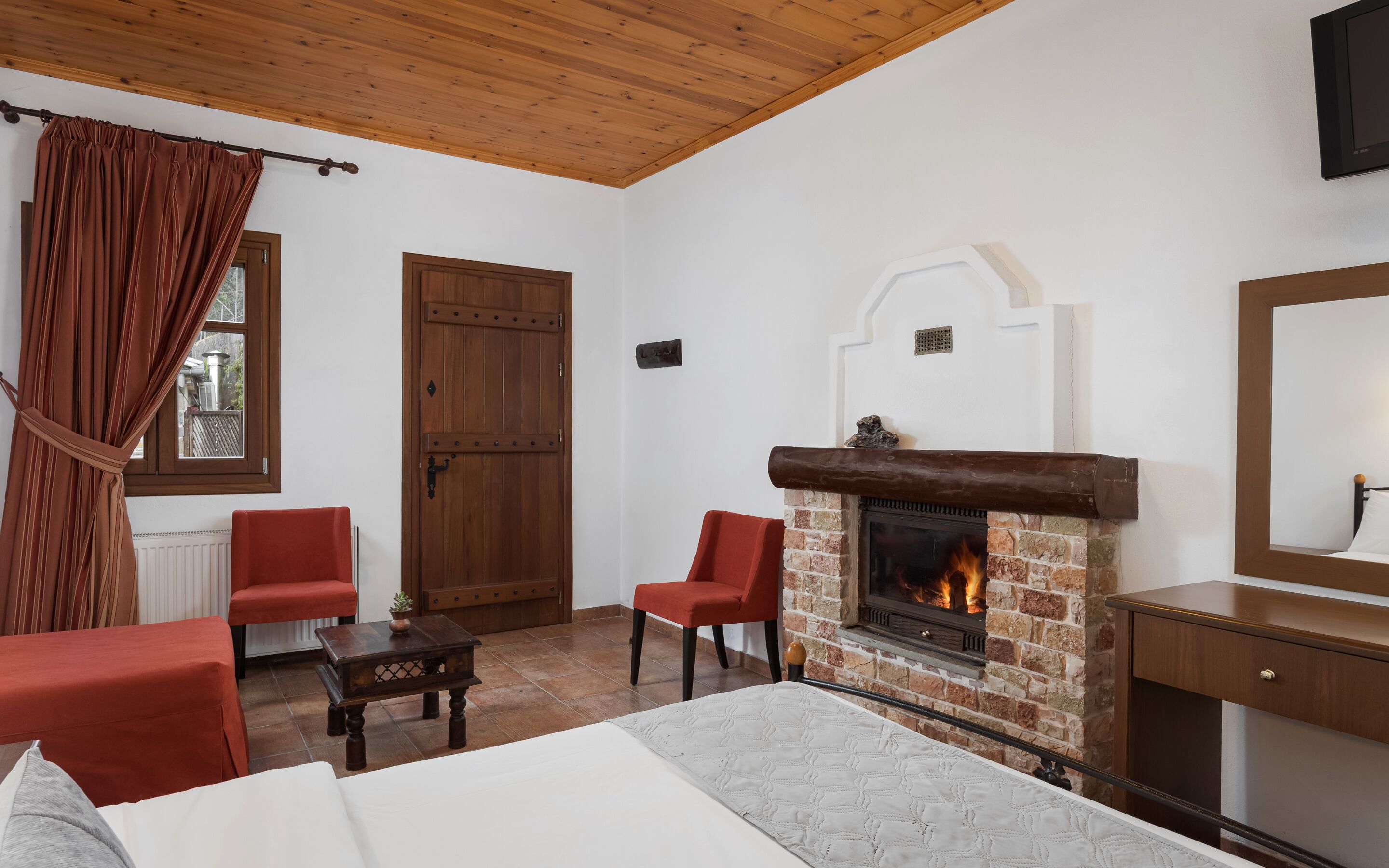 A room with a fireplace, a bed, a red chair, and a wooden door.