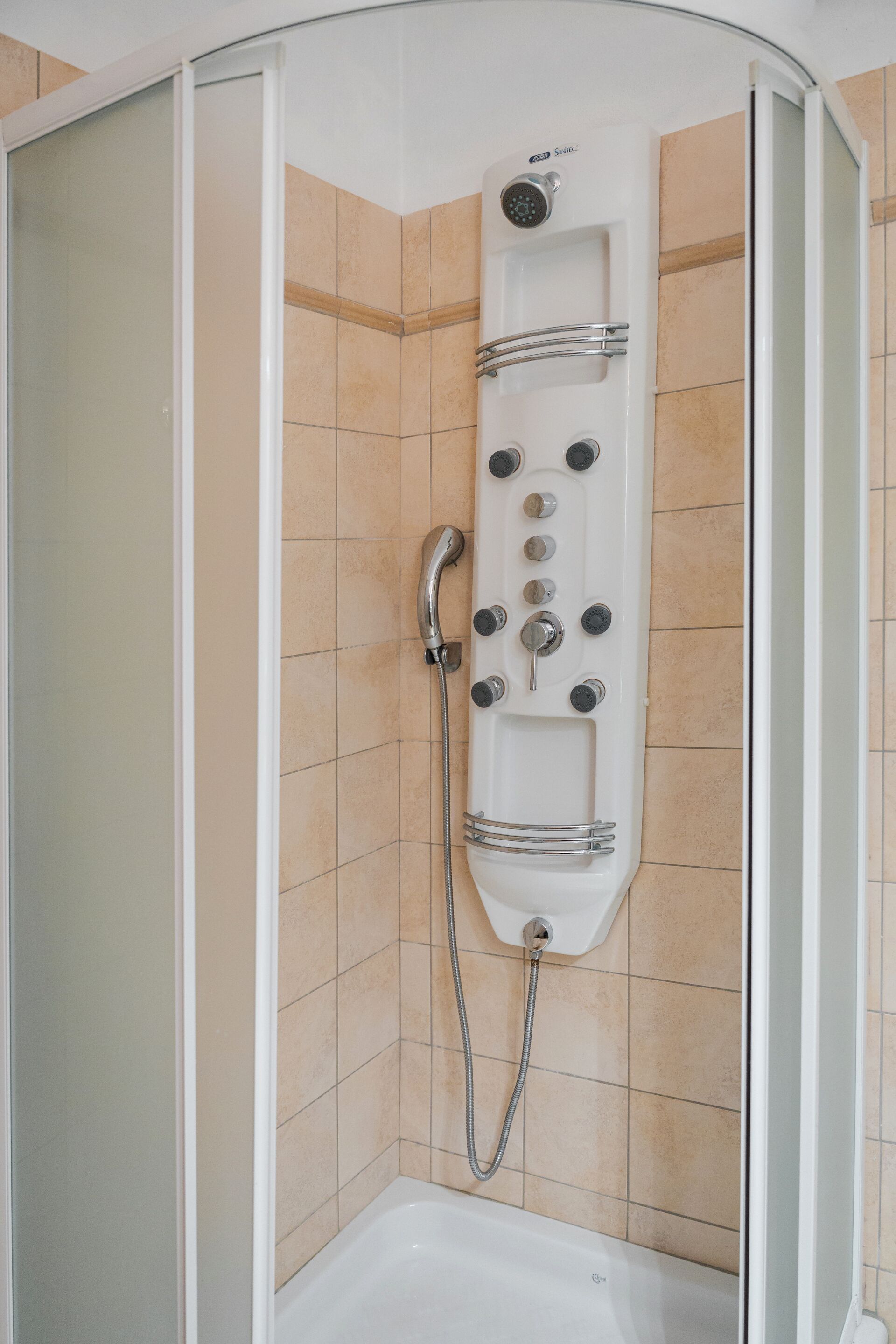 A walk-in shower with a handheld showerhead, multiple control knobs, and a handheld faucet.
