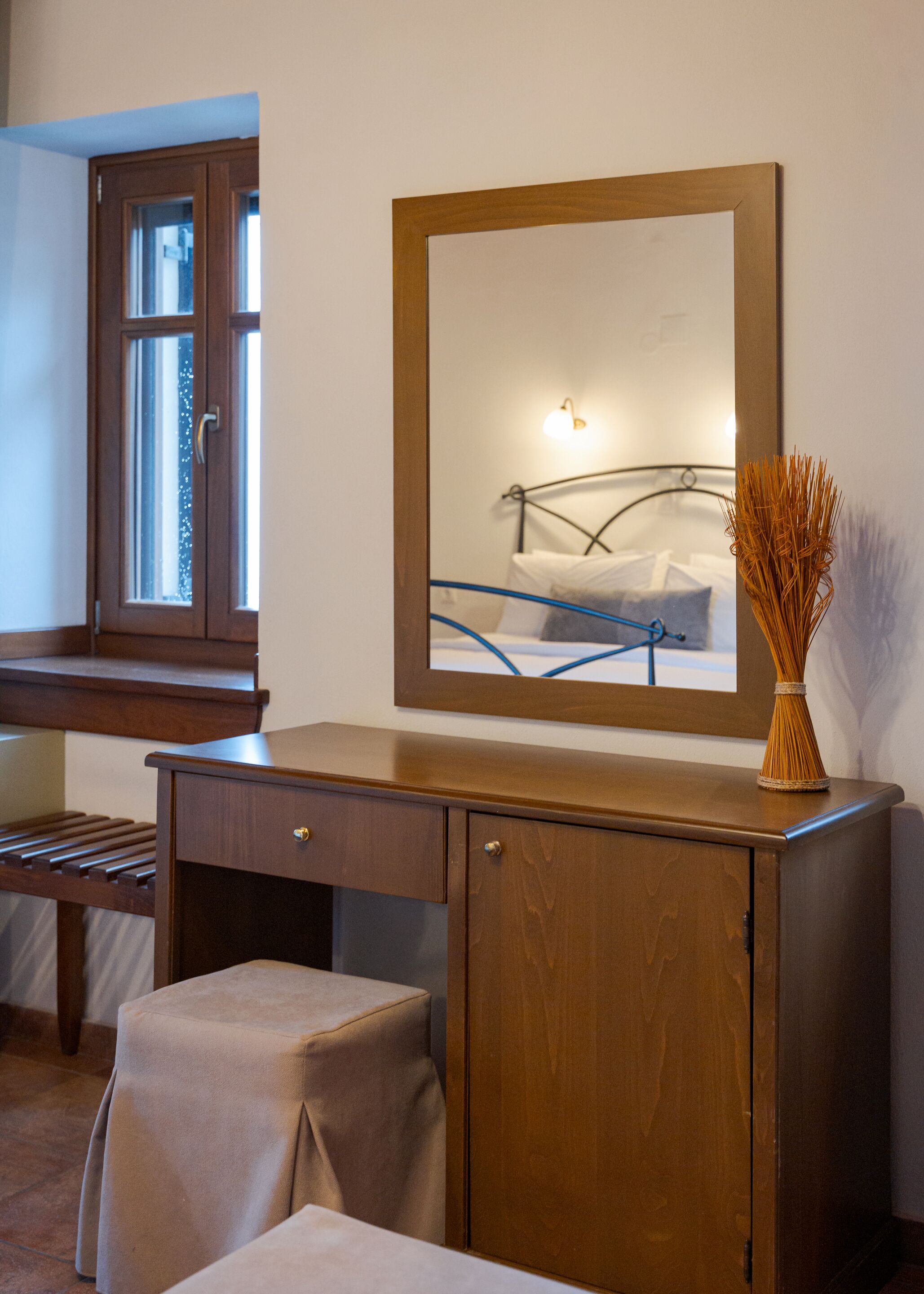 A wooden desk with a mirror, a vase, and a bed with a metal frame.