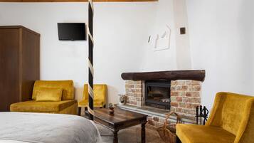 Una habitación acogedora con una cama, dos sillones amarillos, una mesa de madera, una chimenea y un televisor montado en la pared.