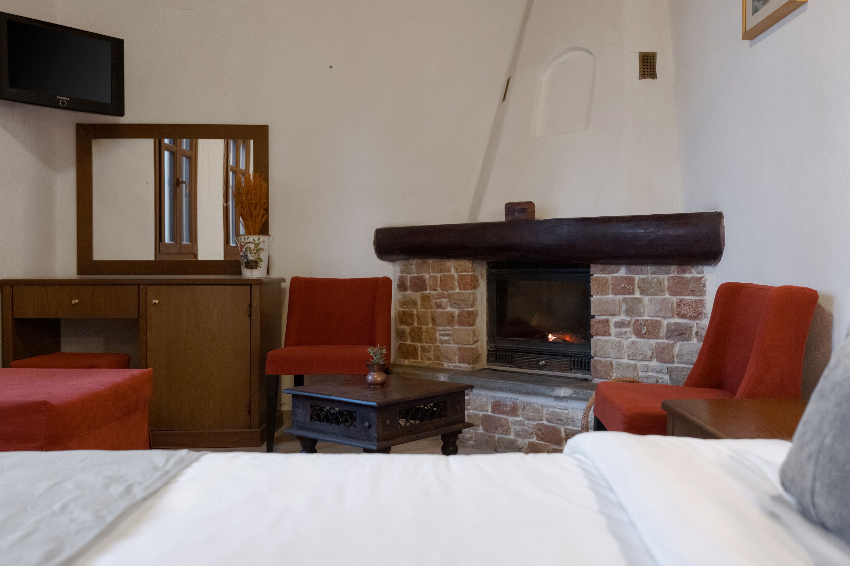 Ein gemütliches Zimmer mit Kamin, einem Bett, zwei roten Sesseln, einem kleinen Tisch und einem an der Wand befestigten Fernseher.