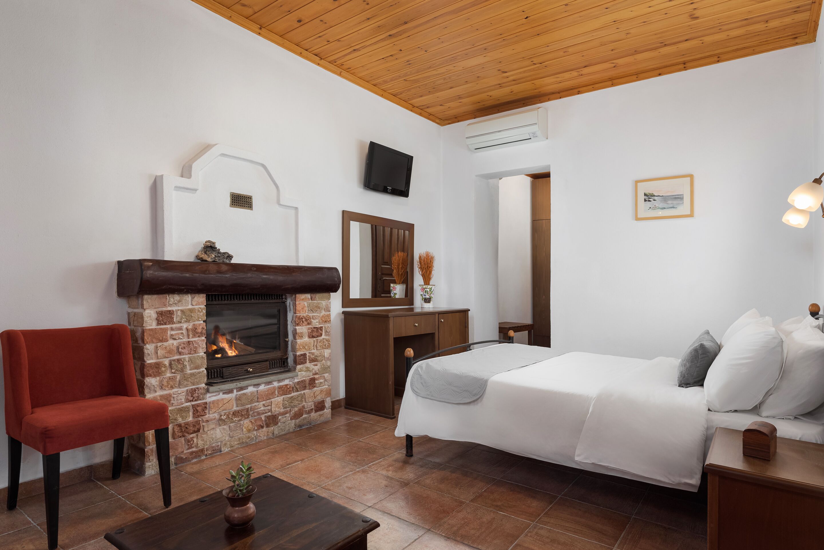 Ein Schlafzimmer mit Kamin, einem Bett, einem Sessel und einem kleinen Tisch.