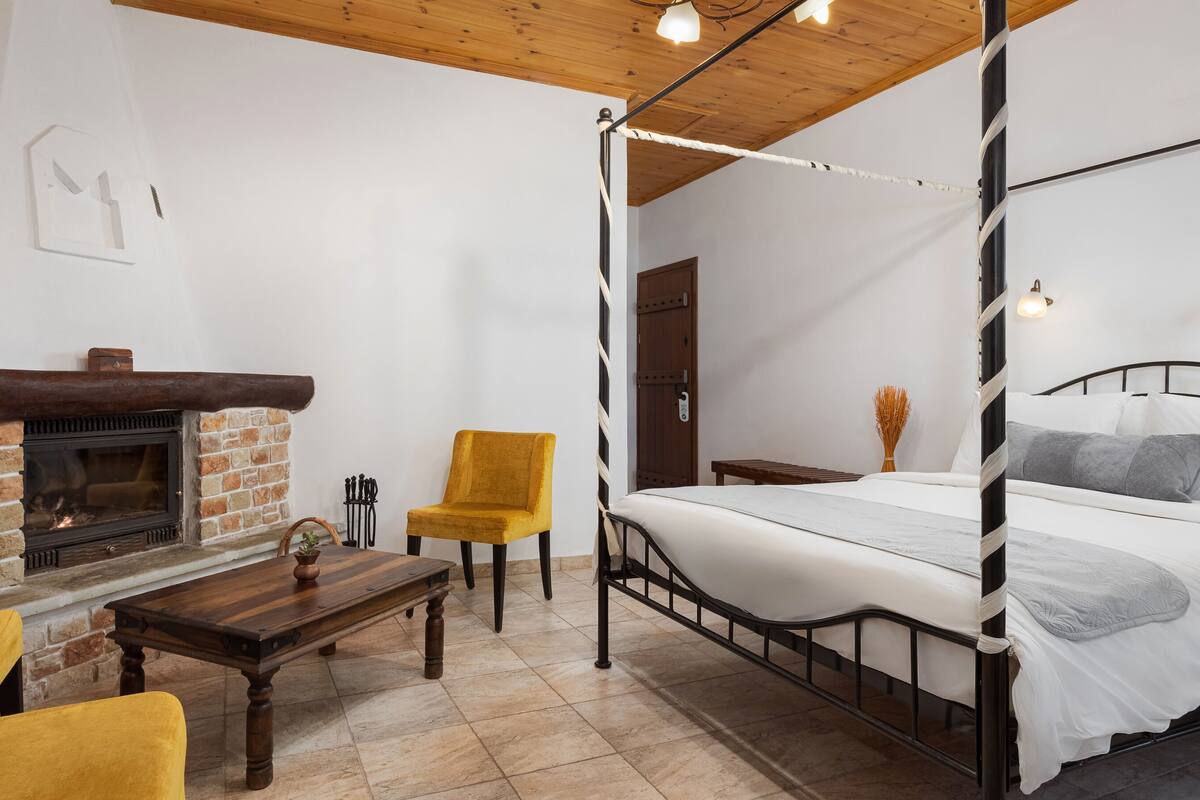 Ein Schlafzimmer mit einem Himmelbett, einem Holztisch, einem gelben Stuhl, einem Kamin und einer Tür.