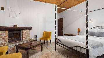A bedroom with a four-poster bed, a wooden table, a yellow chair, a fireplace, and a door.