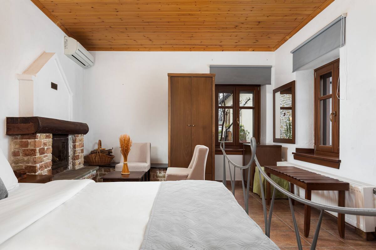 Ein Schlafzimmer mit Kamin, einem Bett, einem Sessel, einem Tisch und Blick ins Freie.