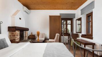 A bedroom with a fireplace, a bed, a chair, a table, and a view of the outside.