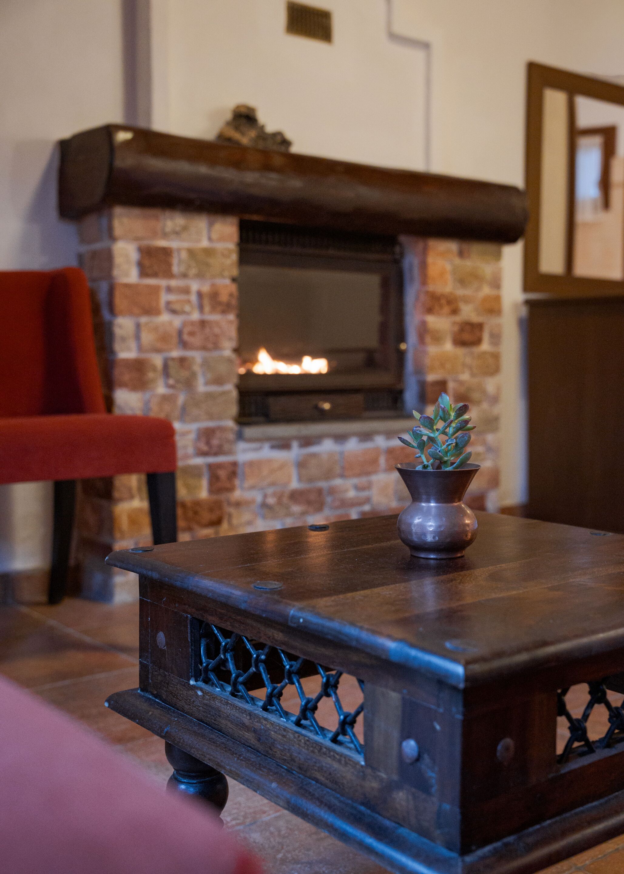 A wooden table with a metal grille, a potted plant, and a brick fireplace in the background.