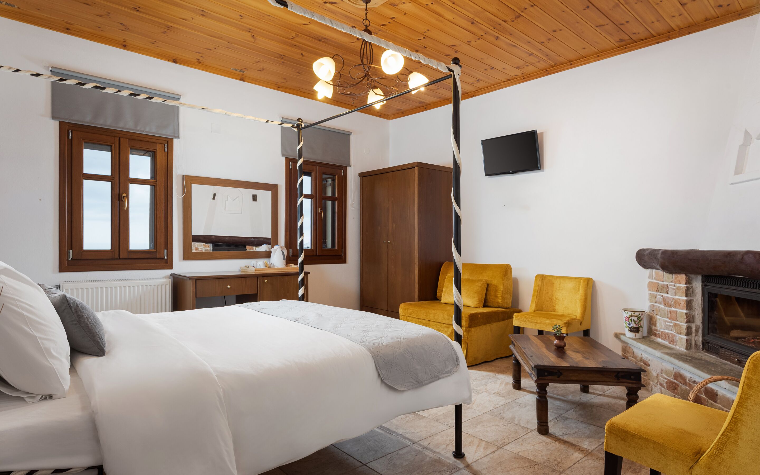 A bedroom with a bed, a wooden wardrobe, a television, a fireplace, and a small table.