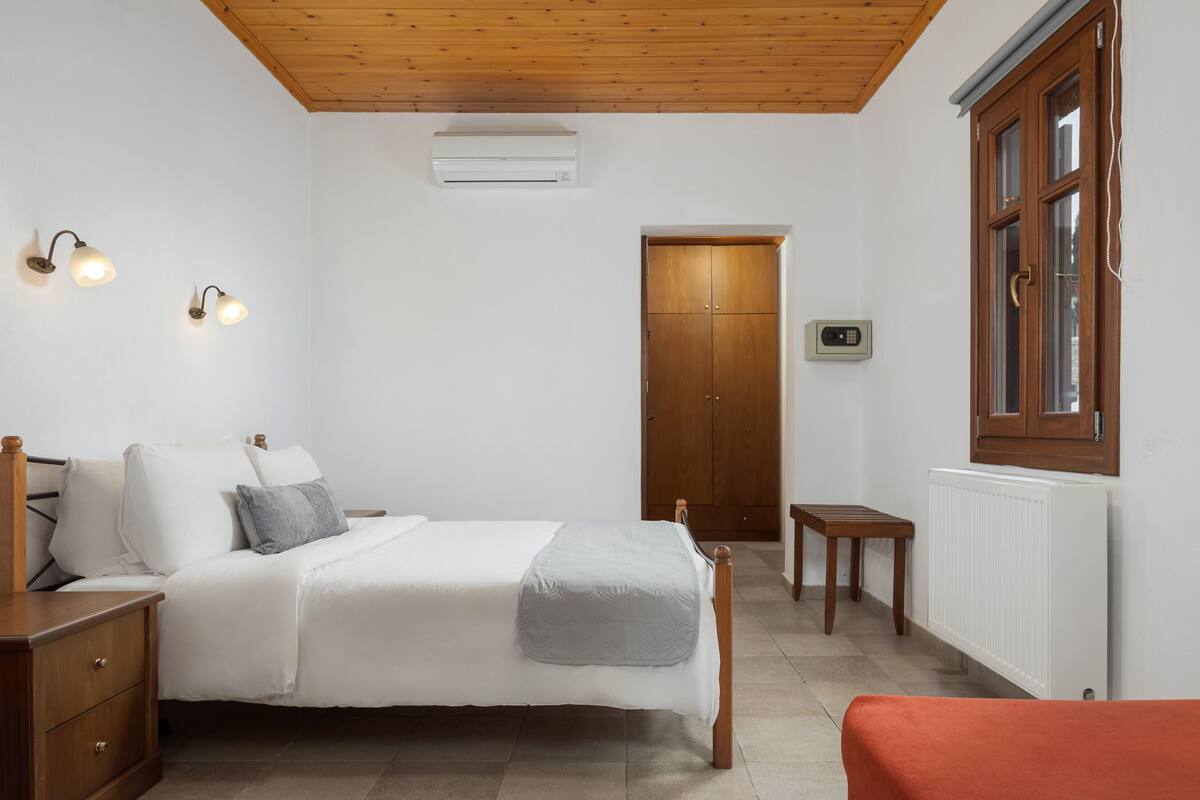 Ein Schlafzimmer mit einem hölzernen Bett, Nachttischen, einem Kleiderschrank, einem Heizkörper und einem Fenster mit Vorhängen.