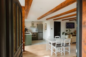 Eine moderne Küche mit weißen Schränken, einem Edelstahl-Kühlschrank und einem Essbereich mit weißen Stühlen und einem Tisch.