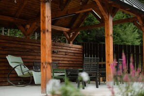 Eine Holzupergola mit überdachter Terrasse, inklusive Schaukelstuhl und mehreren Sitzgelegenheiten.