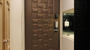 Eine braune Tür mit einer strukturierten Oberfläche, ein kleines elektronisches Gerät an der Wand und ein gemustertes Teppich