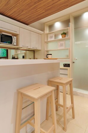 Une cuisine moderne avec des meubles blancs, un four à micro-ondes et deux tabourets en bois.