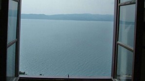 Blick durch ein Fenster auf einen klaren Himmel und ruhiges Wasser, möglicherweise ein See oder Meer, mit unscharf erkennbaren Landformen in der Ferne.