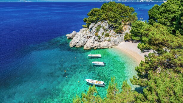 A coastal scene with clear turquoise waters, rocky outcrops, and boats anchored near the shore.