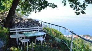An outdoor seating area with a table and chairs, a stone wall, and a view of the sea.