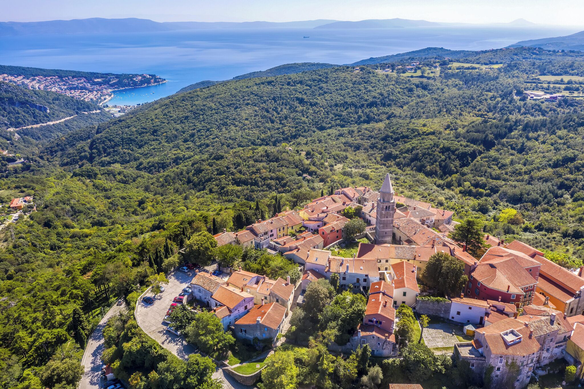 An aerial view of a coastal town with a prominent church, surrounded by lush greenery and a clear blue sea.