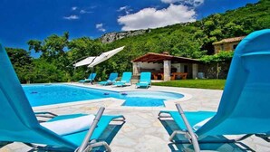 Une piscine avec des chaises longues, un espace de détente abrité et un paysage montagneux en arrière-plan.