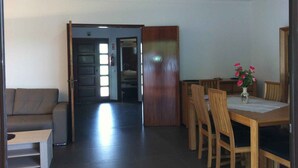 Een woonkamer met een bank, een eettafel met stoelen en een zichtbare keuken door een open deur.