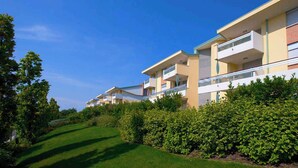 Una hilera de edificios residenciales modernos, de varios pisos, con balcones, rodeada de céspedes cuidados y abundante follaje.