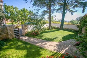 A well-maintained garden with a stone pathway, lush green lawn, and various plants. - Holiday apartment with balcony (Novigrad)