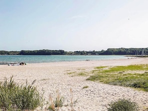 Une plage de sable avec un quai, une eau calme et une ligne d’arbres à l’horizon.