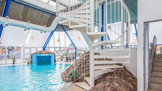 Una piscina interior con pared de piedra y una escalera en espiral blanca.