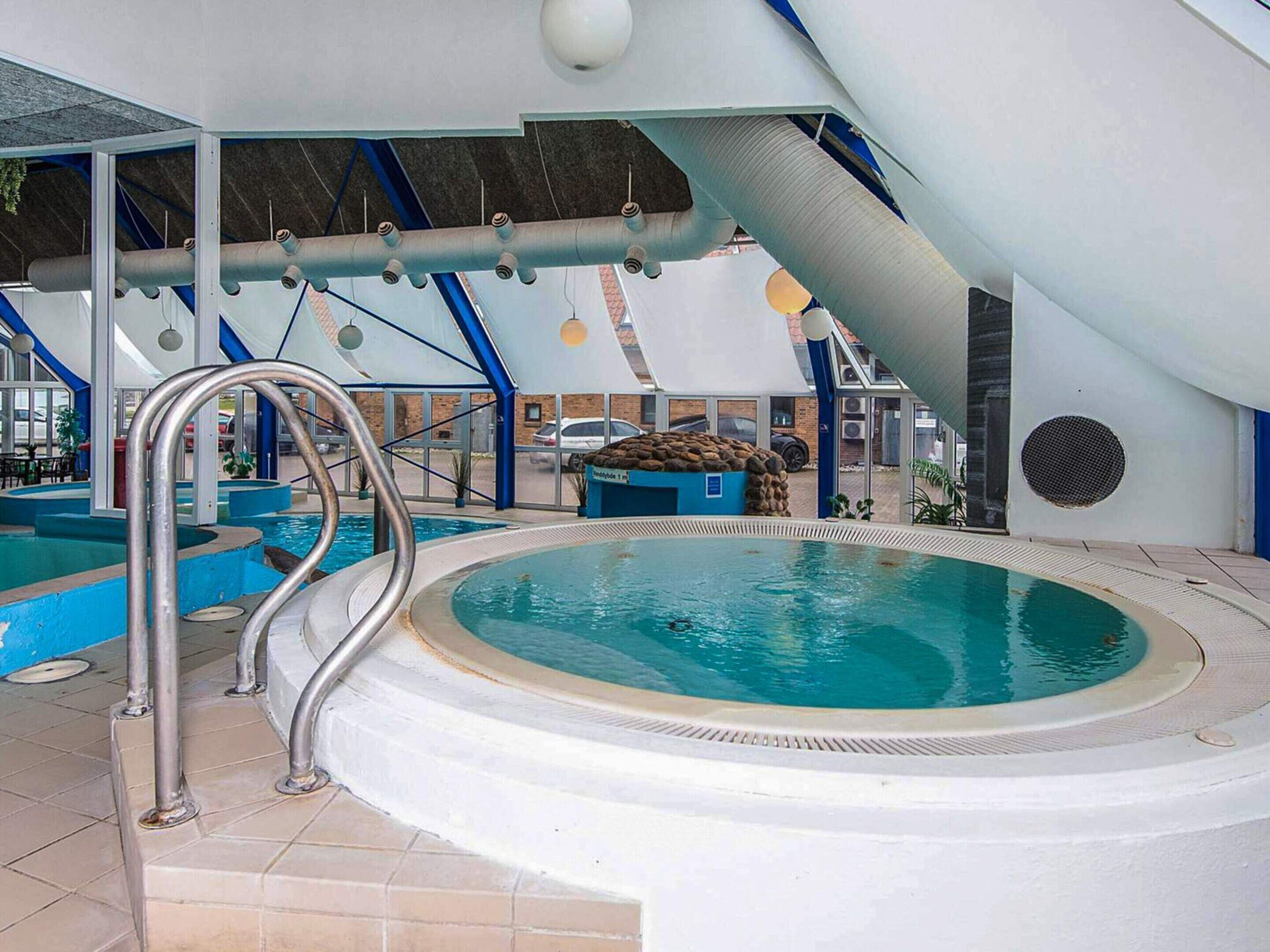 Ein Innenpool mit Whirlpool, umgeben von einer überdachten Fläche mit geneigtem Dach und großen Fenstern.
