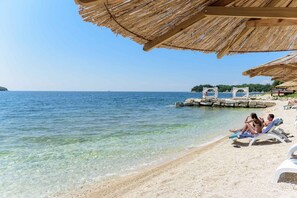 A beach with clear water, a thatched roof structure, and a small pier. - Holiday apartment with air conditioning and balcony (Funtana)