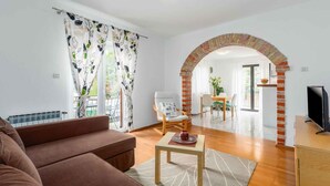 Una sala de estar con un sofá marrón, una mesa de centro de madera y un arco de ladrillo que conduce a un comedor.