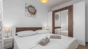 Una cama bien hecha con sábanas blancas y dos toallas enrolladas, una lámpara de noche y un espejo en la puerta del armario.