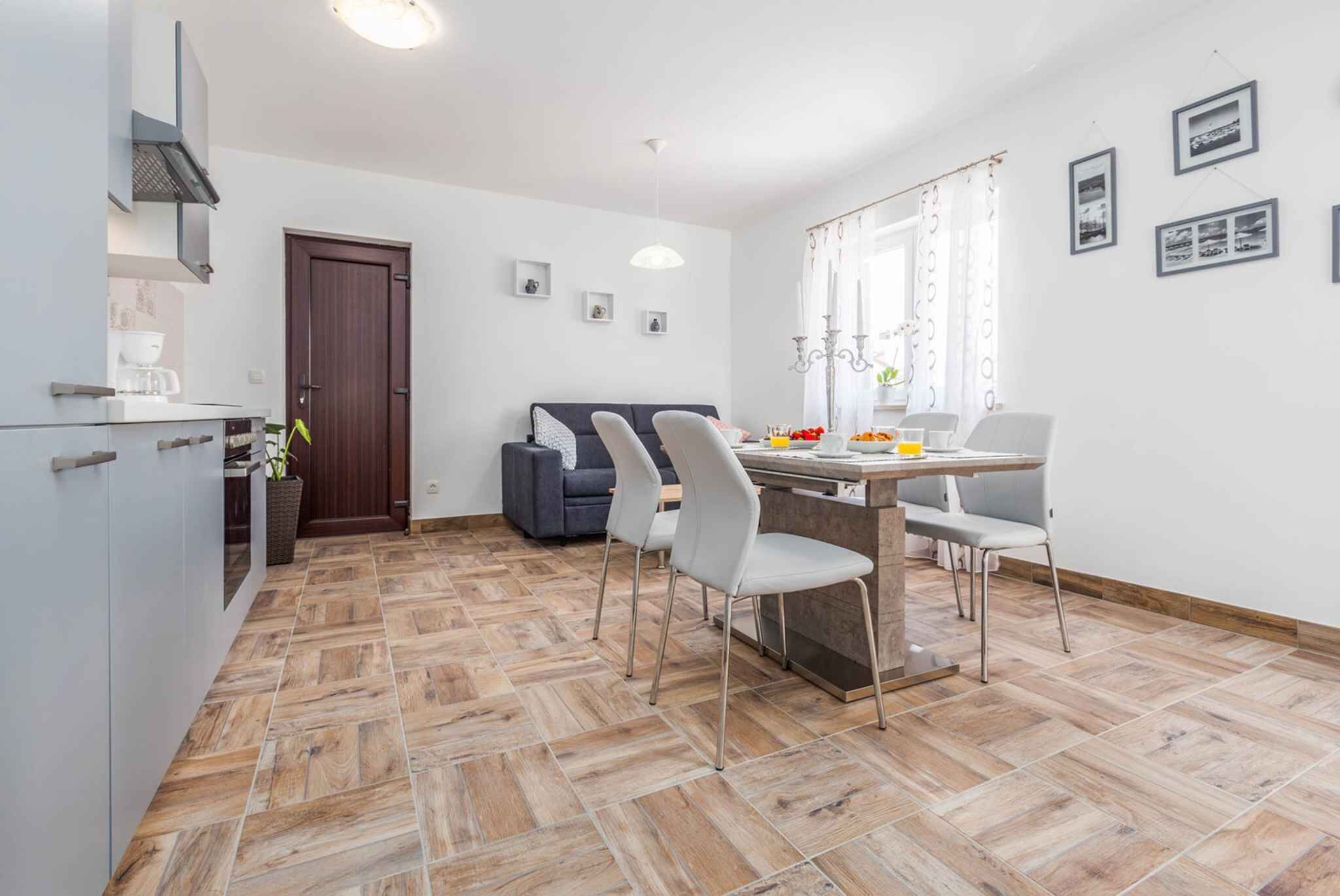 A modern kitchen with a dining area, featuring a herringbone floor pattern, a dark wooden door, and a dining table with chairs.