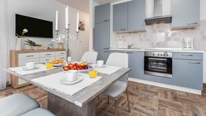 Una cocina moderna con armarios grises, horno integrado y comedor con mesa y sillas de mármol.