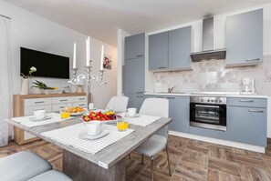 A modern kitchen with grey cabinets, a built-in oven, and a dining area with a marble table and chairs. - Holiday apartment with air conditioning and terrace (Funtana)